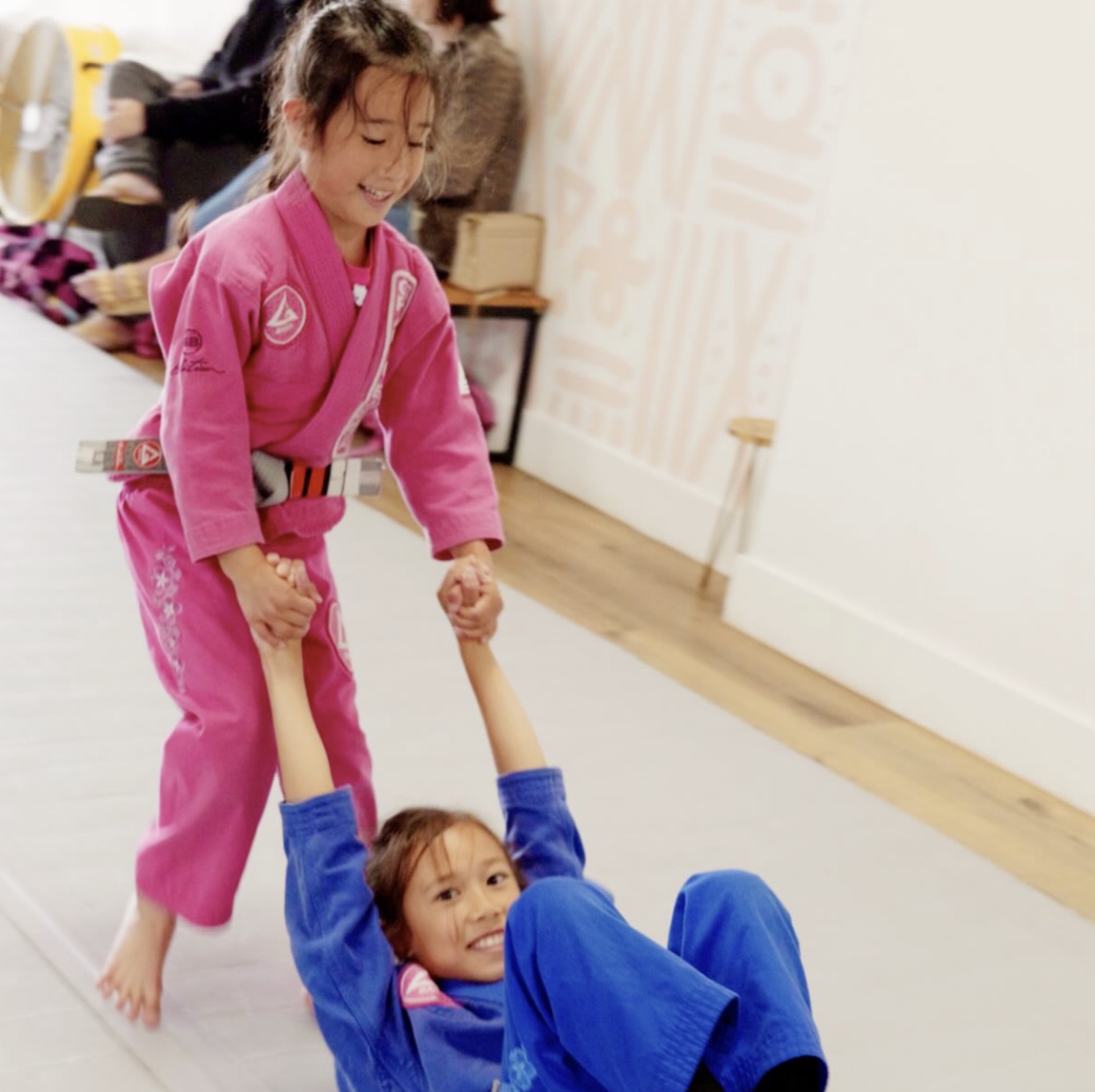 Two young students in pink and blue gis in front of the patterned mural