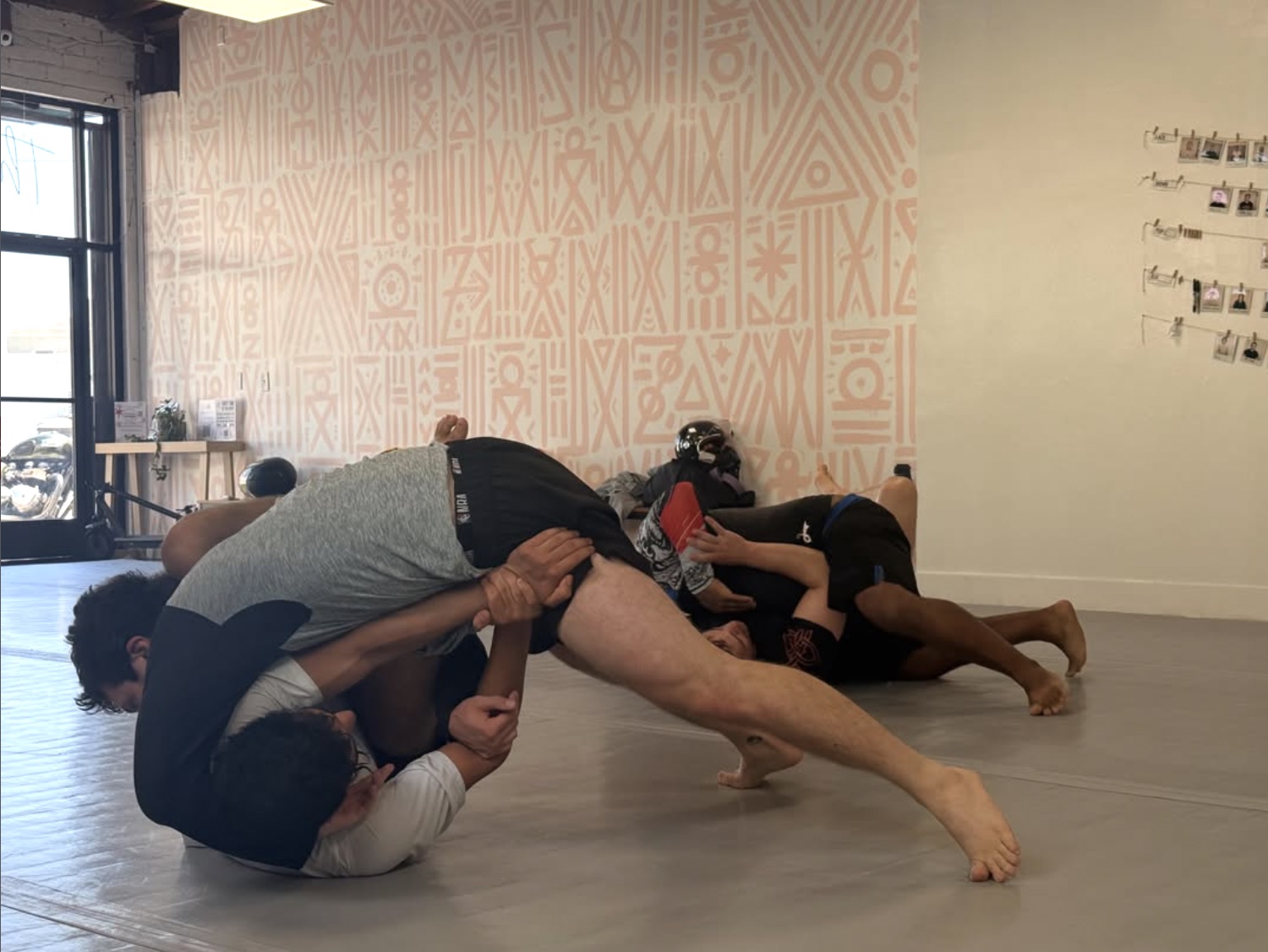 A no-gi scramble in front of the dusty-pink geometric mural