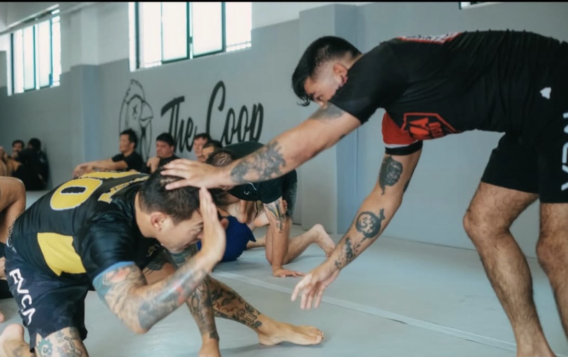 A no-gi wrestling scramble by the wall with the rooster logo mural